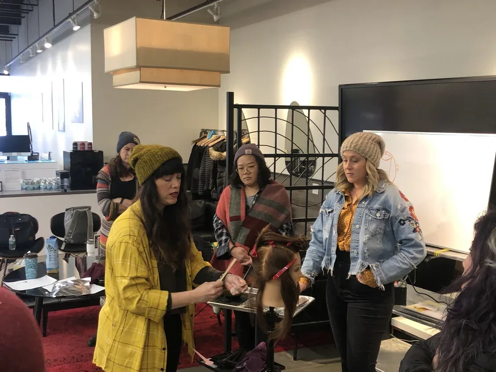 An educator demonstrating a technique on a mannequin head while stylists look on.