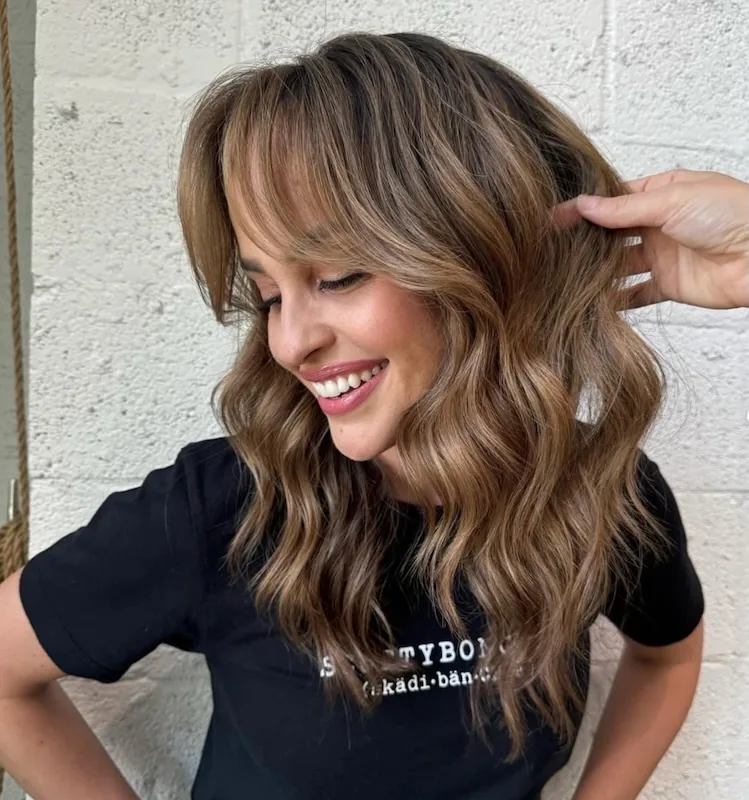 Bronde balayage with curtain bangs and soft waves, in the studio tee.