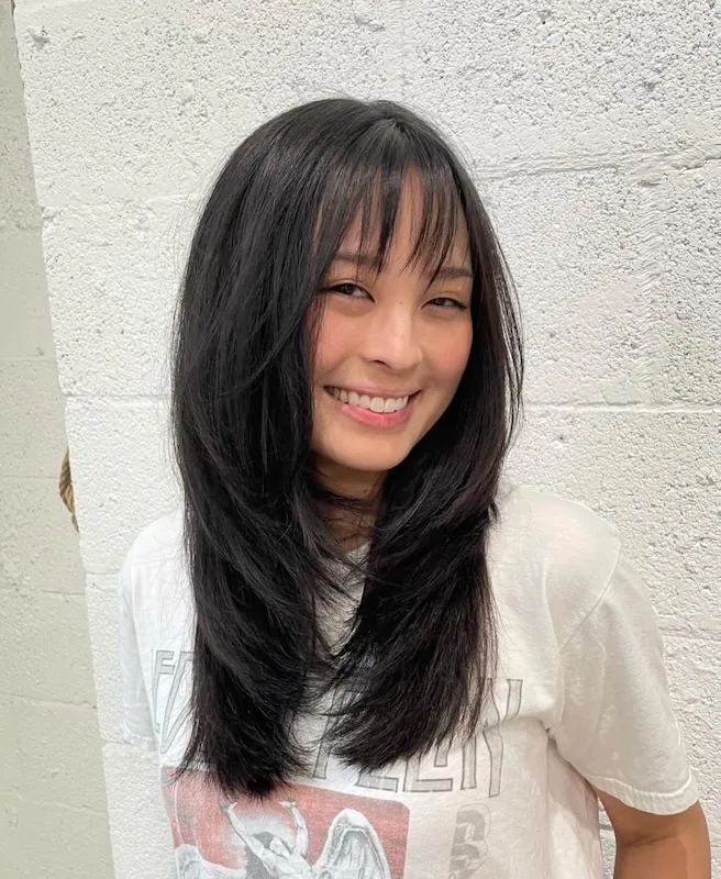 Long black layered cut with wispy bangs, worn sleek and smooth.