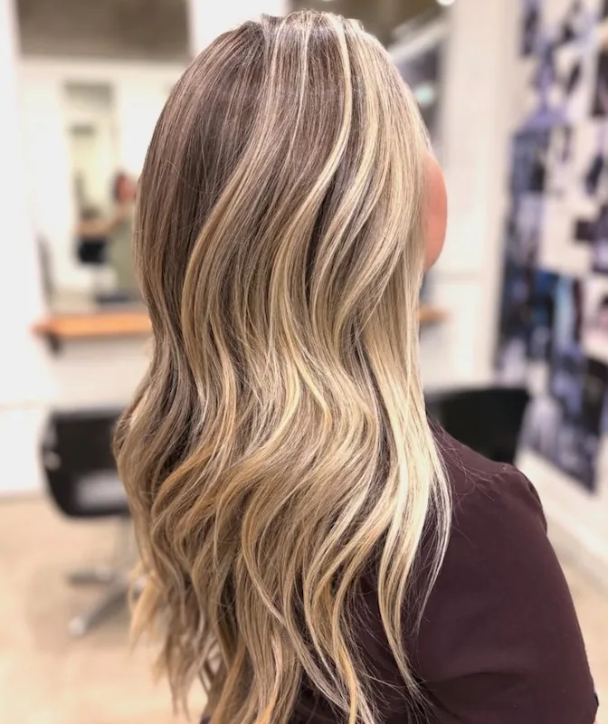 Dimensional blonde balayage ribbons over a deep shadow root, in long waves.