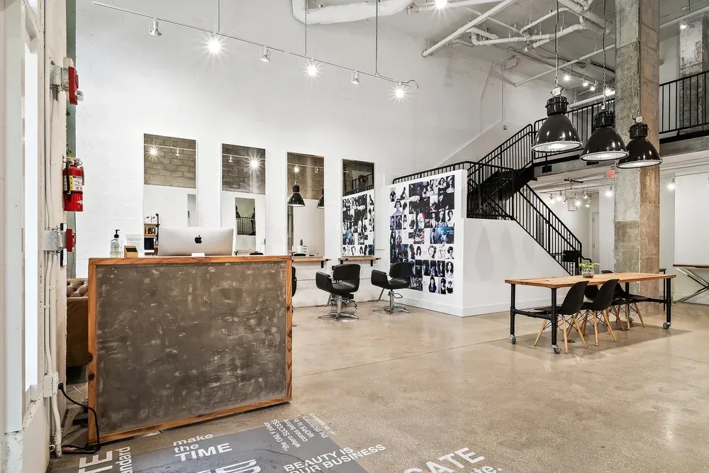 The full salon floor: polished concrete, a communal wood table and the black steel loft staircase.