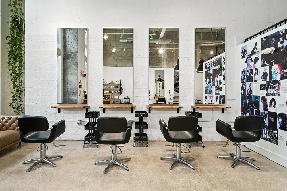 Styling stations with tall mirrors and black chairs along the photo-collage wall at Scotch Bonnet, a hair salon in downtown West Palm Beach.