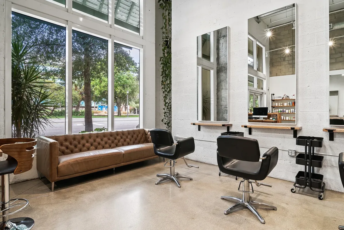 A tufted leather sofa and styling chairs beside the wall of windows at the West Palm Beach salon.